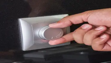 A hand adjusts a silver circular dial on a square wall-mounted control panel.
