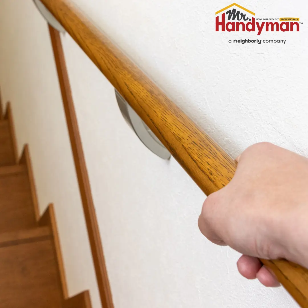 A person hold a polished wooden handrail mounted on a white wall.