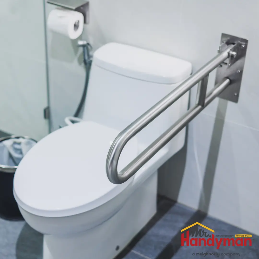 A modern white toilet with a stainless steel, wall-mounted flip-up grab bar.