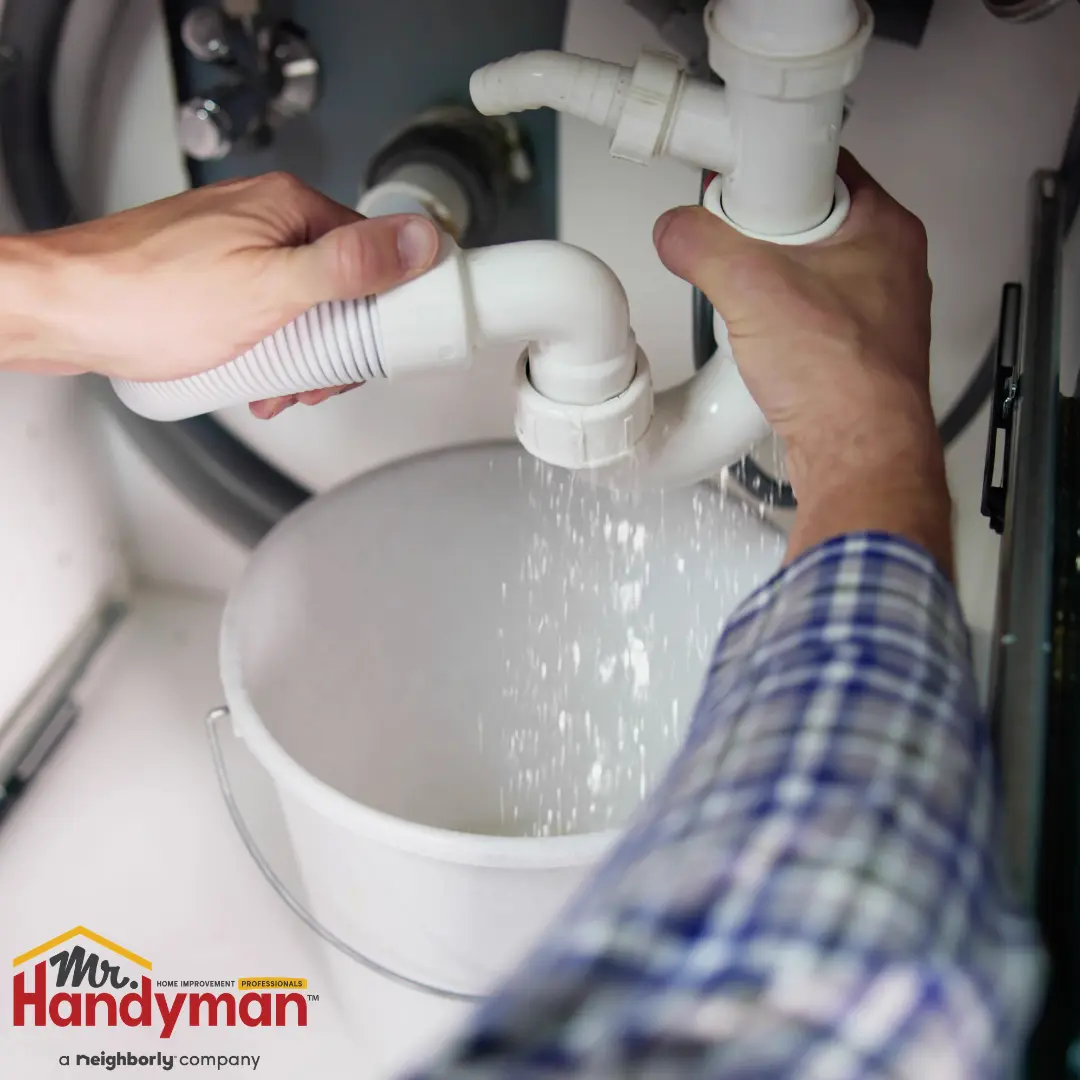 A person fixing a plumbing issue, with water flowing from a pipe into a bucket.