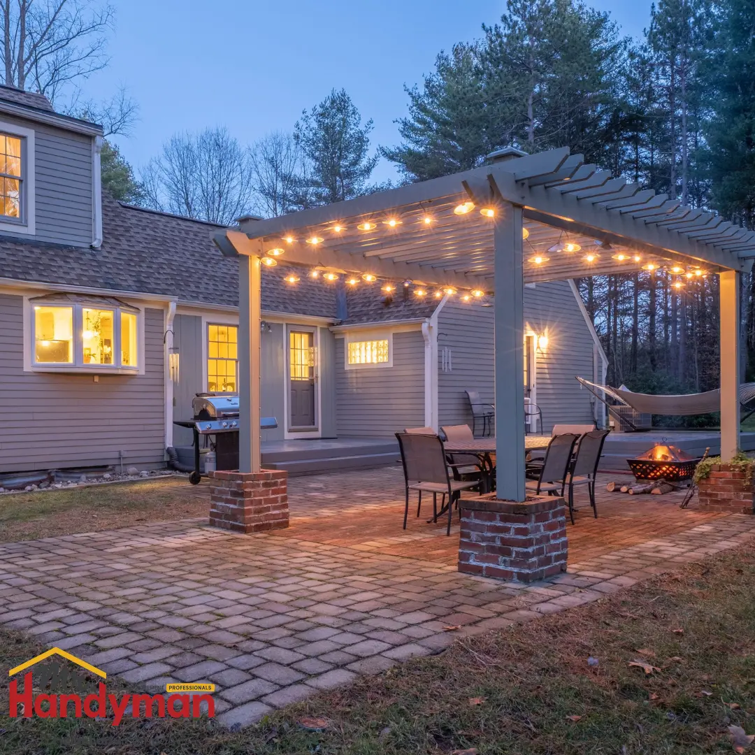A cozy backyard patio area with string lights, a stone pathway, and a seating arrangement near a fire pit, surrounded by trees.
