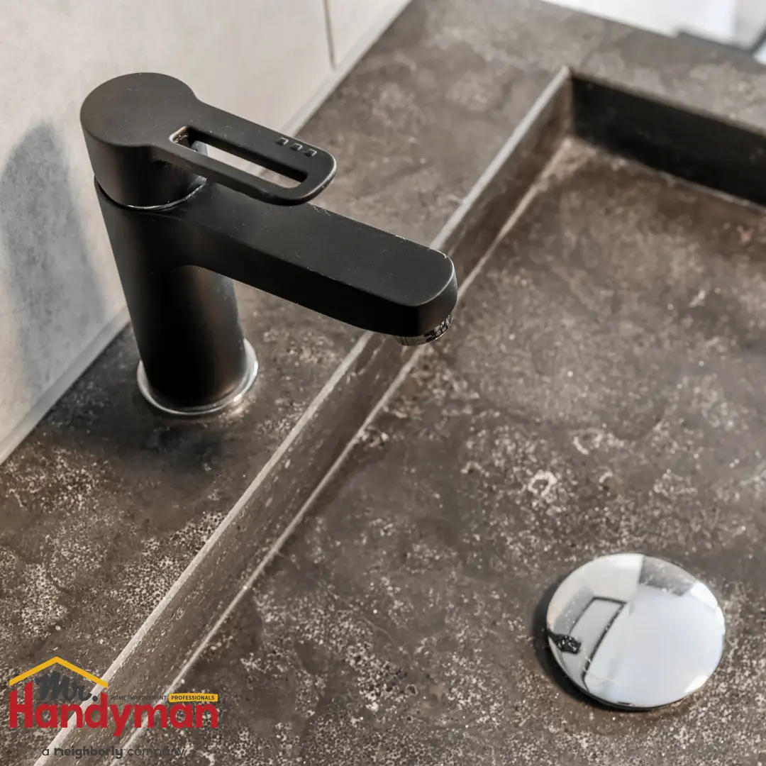 A modern matte black single-handle bathroom faucet installed on a dark stone countertop with a built-in sink.