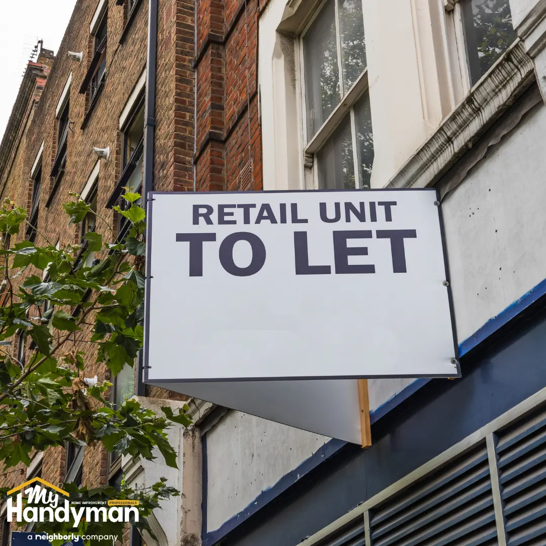 Sign reading "Retail Unit To Let" hanging on exterior of brick building.