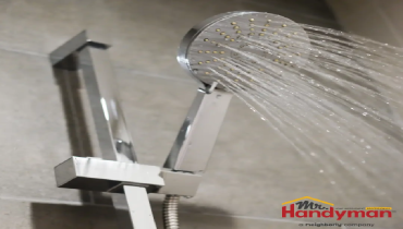 A modern chrome handheld shower head spraying water in a tiled bathroom.