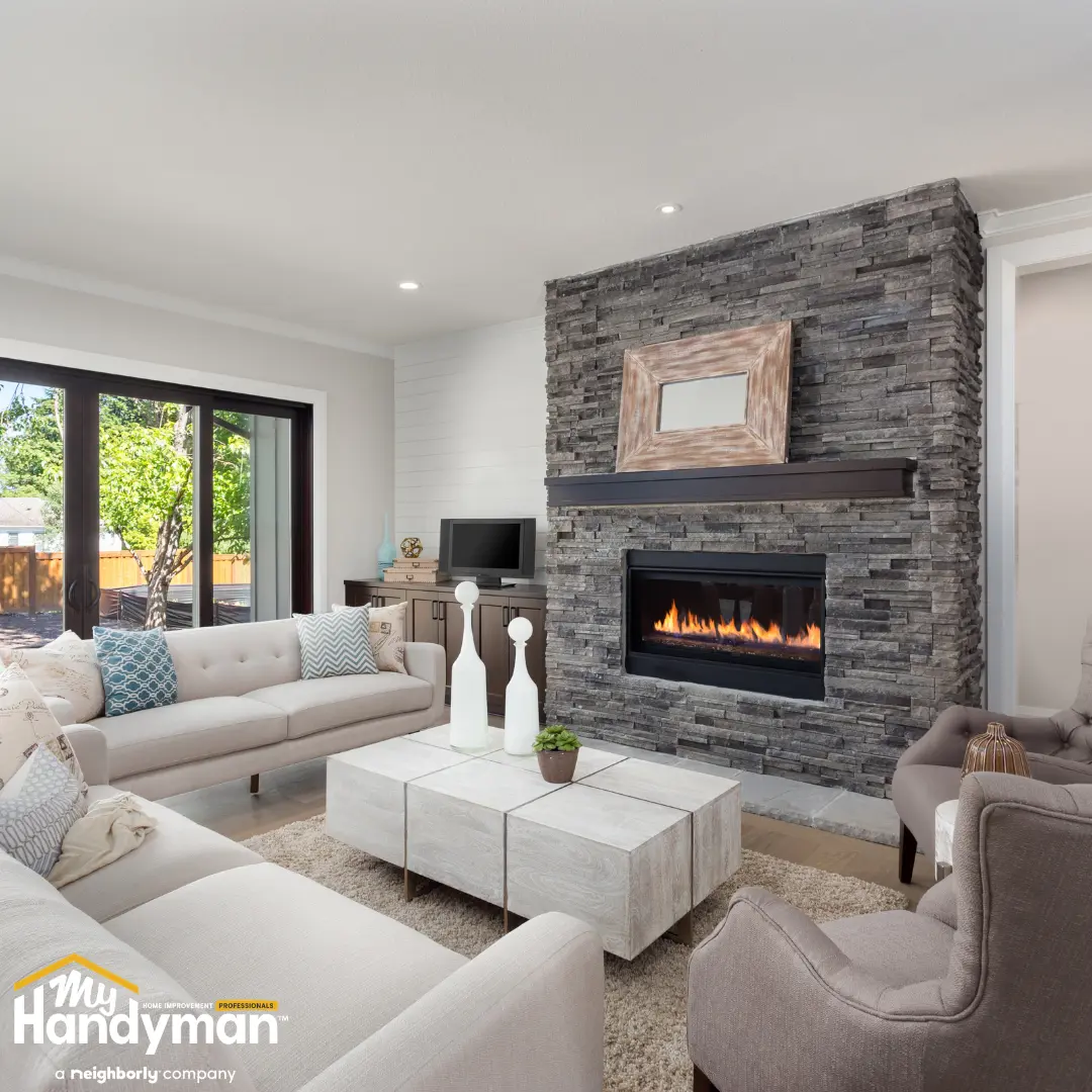 Living room with light-colored sofas, armchairs and a stone fireplace with a lit fire.