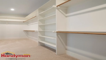 A neatly organized walk-in closet with white shelving, wooden hanging bars, and a carpeted floor.