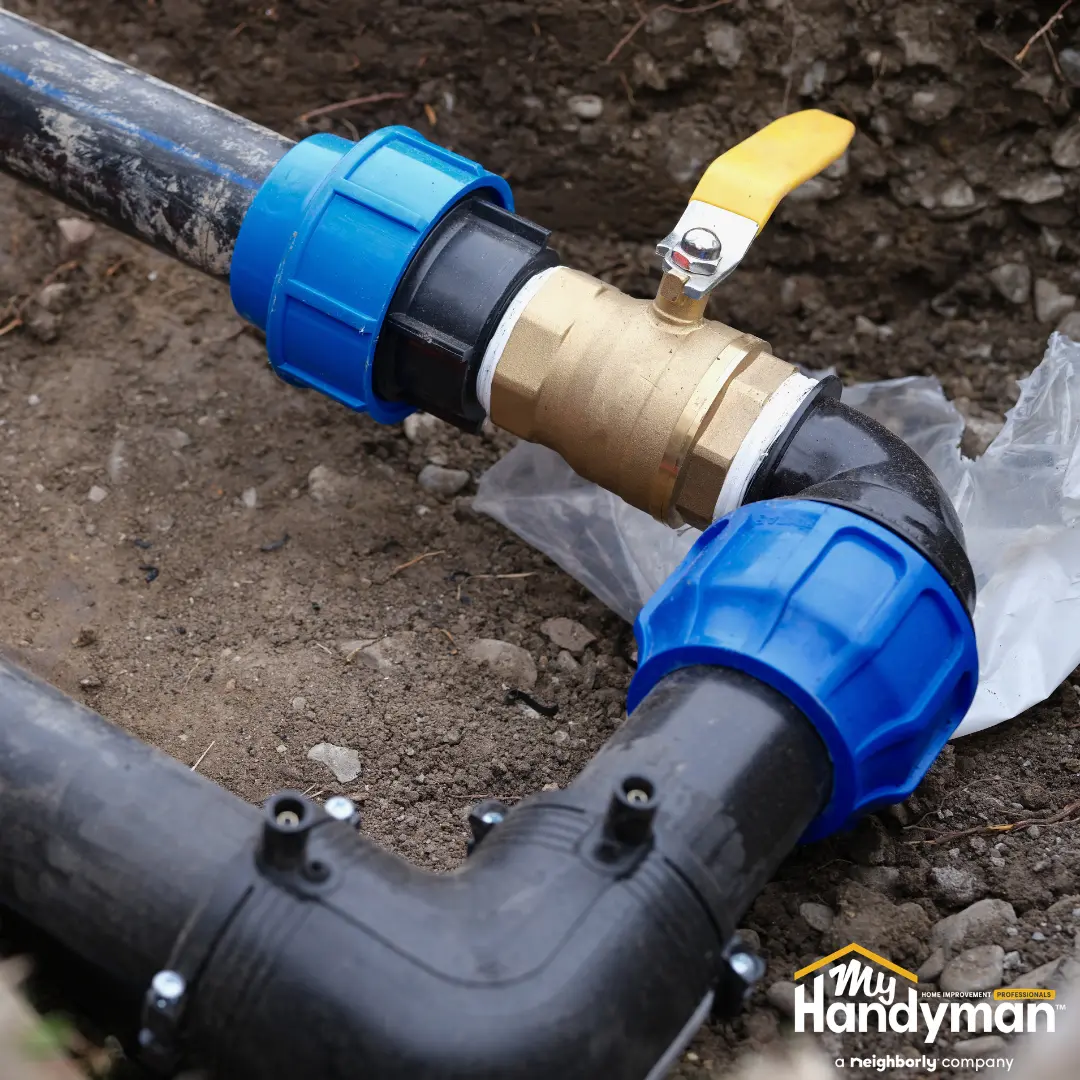 Close-up of underground black plastic pipes connected by a brass valve.