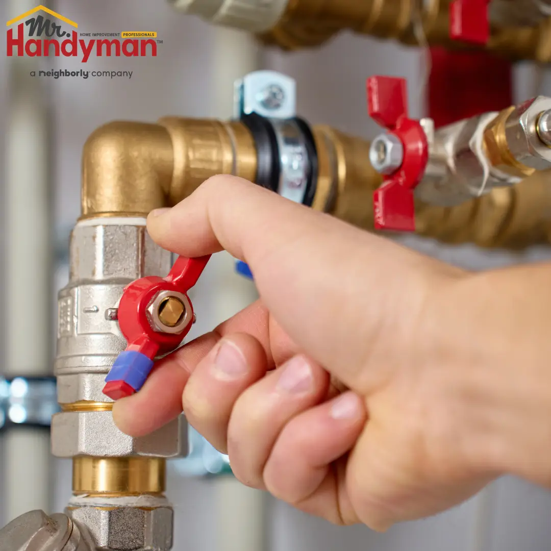 A person turning a red-handled valve on a brass and metal plumbing system, likely to shut off water or gas supply.