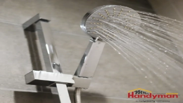 A modern chrome handheld shower head spraying water in a tiled bathroom.