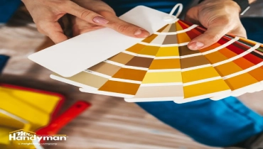Hands holding a color swatch fan with various shades of yellow, orange, and brown.