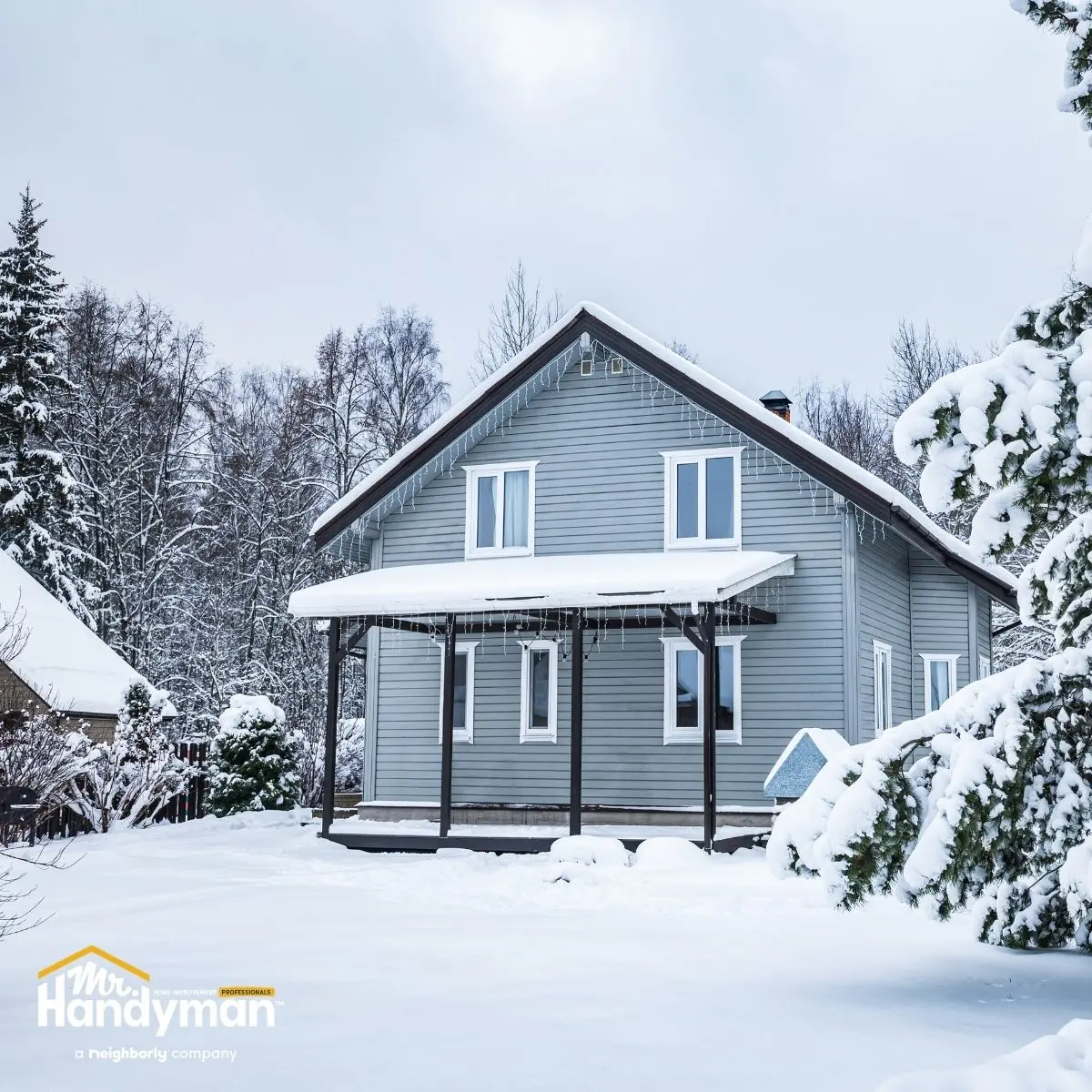 A gray two-story house with a porch, surrounded by snow.