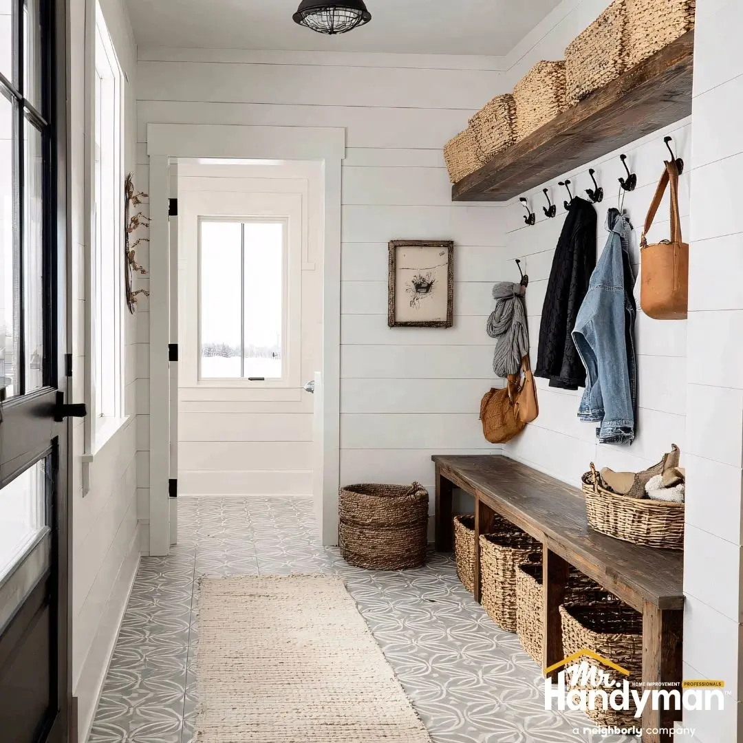 Bright mudroom with white walls, patterned tile floor, wooden bench with baskets, and wall hooks for coats and bags.