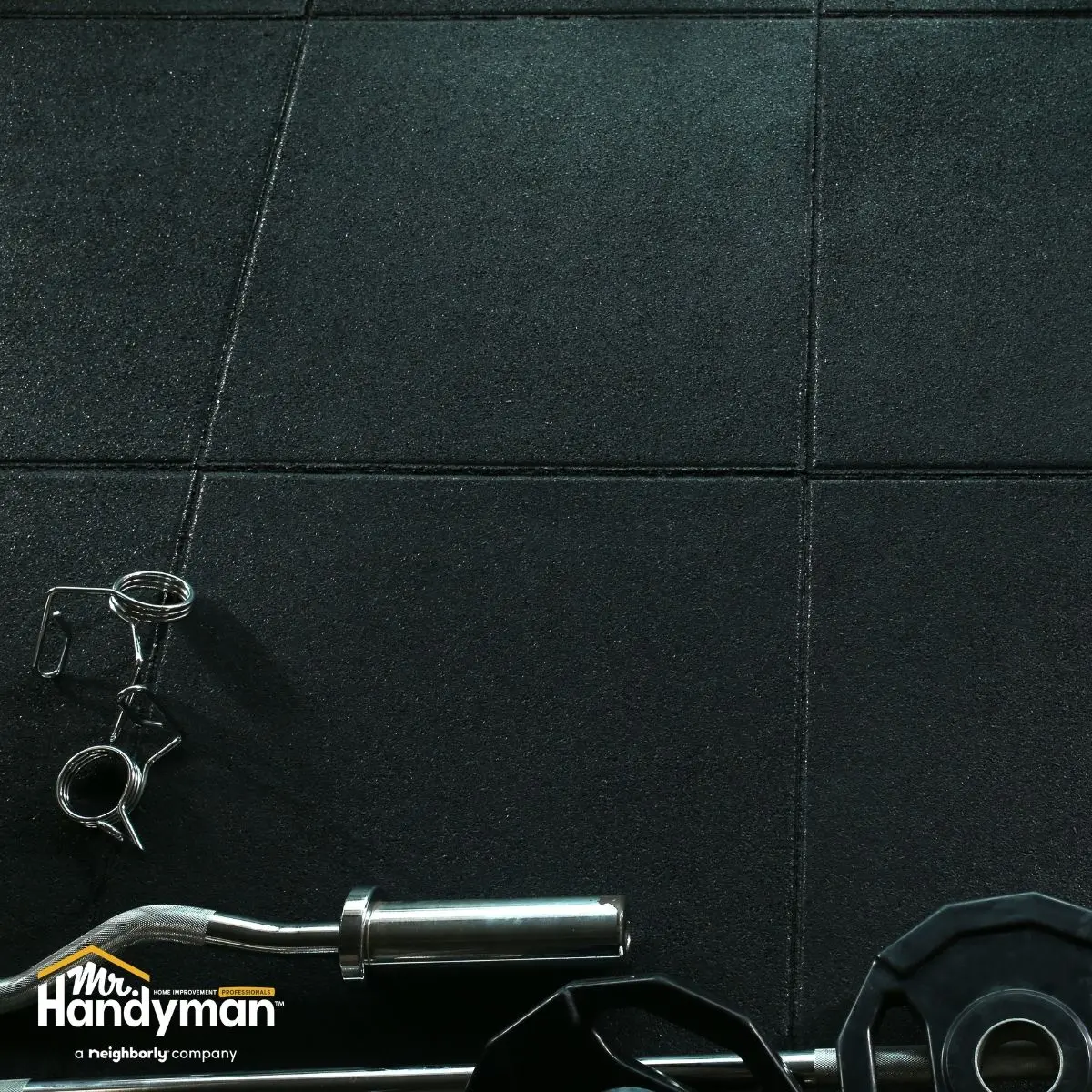Black rubber gym floor tiles with EZ curl bar, spring collars and weight plate on workout mat.