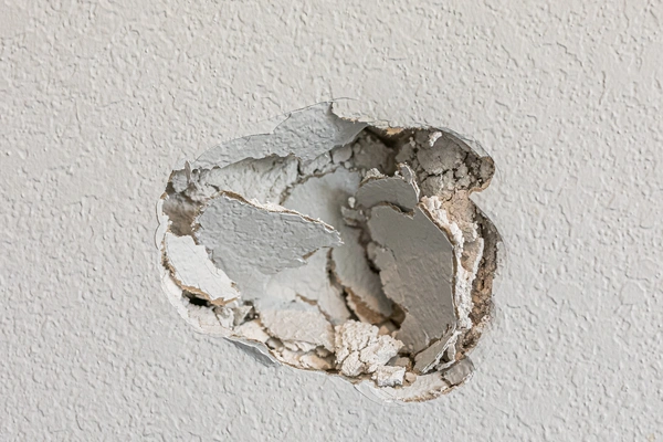 A large, jagged hole broken through a textured drywall.