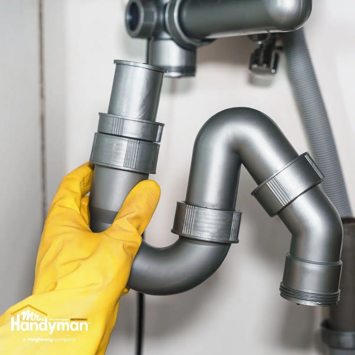 Gloved hand holding a bathroom sink drain pipe under the sink.