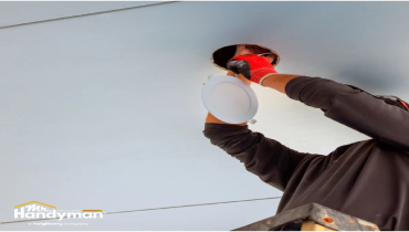 A person installing a recessed light fixture into a ceiling.
