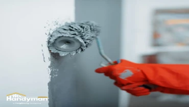 A person wearing red gloves applies gray paint.