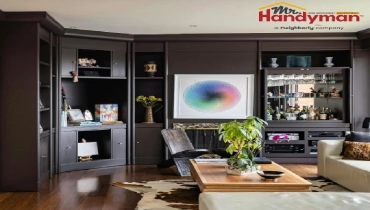 Elegant living room with dark built-in shelving around a fireplace, a glass-front bar cabinet, wooden coffee table, indoor plants, and polished hardwood floors.