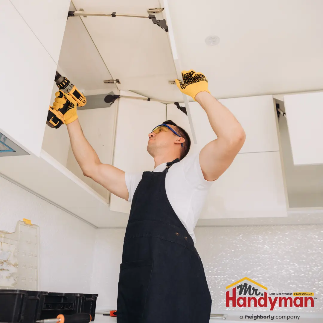 A worker installs or repairs overhead kitchen cabinets.