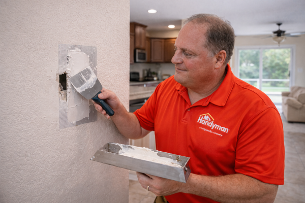 Man repairing a hole in a drywall using a putty knife.
