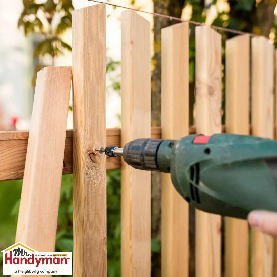 Close-up of fence repair work using a cordless drill on wooden panels.