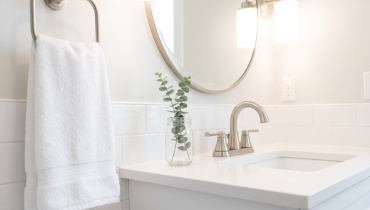 A clean bathroom vanity with a white towel, round mirror, and eucalyptus plant.