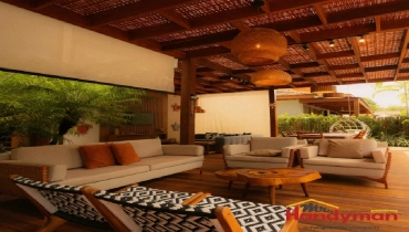A cozy outdoor lounge area with woven ceiling beams, warm pendant lighting, and comfortable seating arranged around a wooden coffee table.