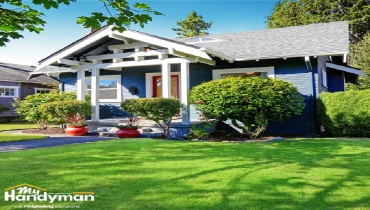 Charming blue house with a welcoming porch, lush green lawn, and vibrant landscaping.