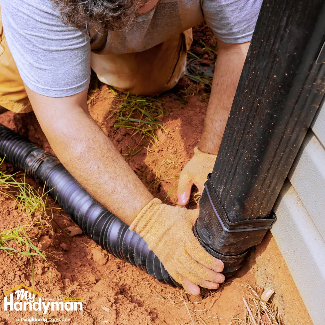 Person connects a drainage pipe to a downspout in a garden.