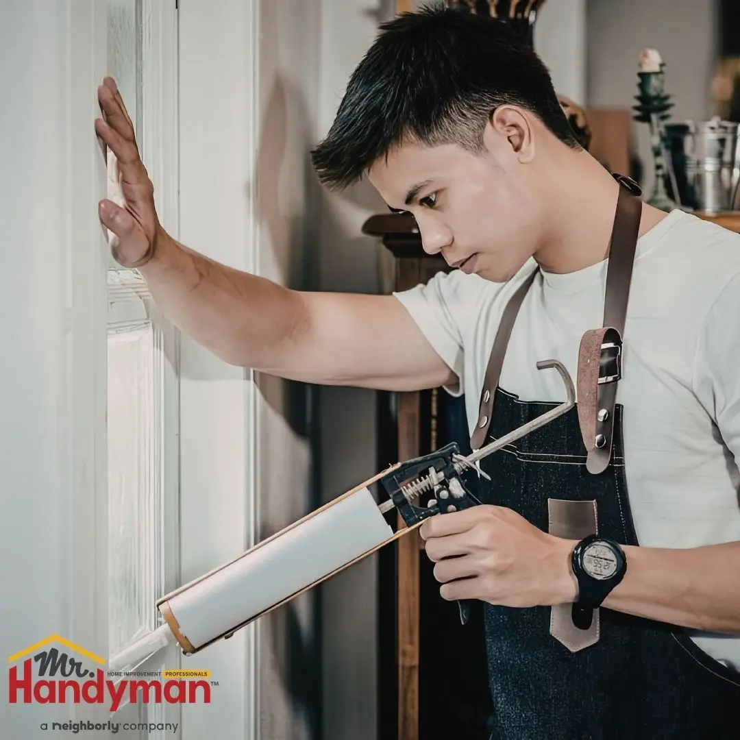 Person using a caulking gun to apply sealant along a window frame.