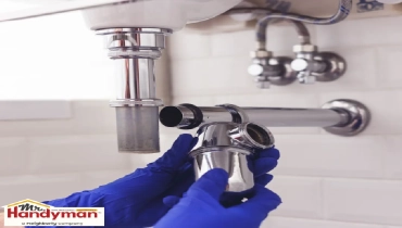 A person is removing a chrome P-trap pipe under a sink.