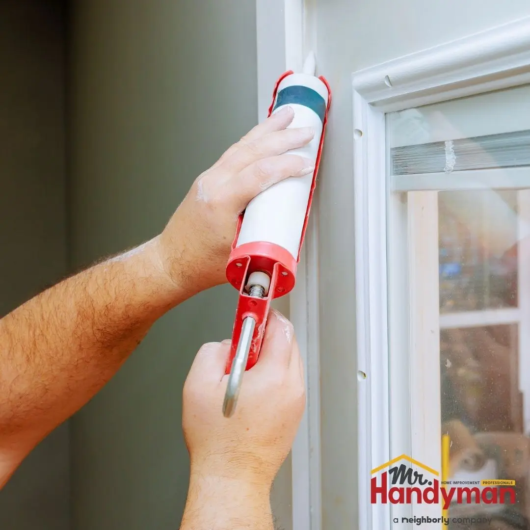 A person using a caulking gun to apply sealant around the corner of a window frame.