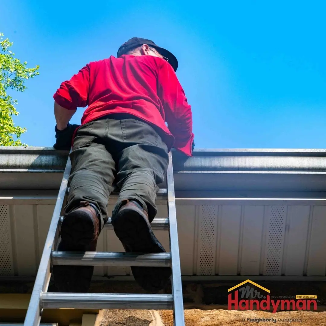 A worker from Mr. Handyman climbing a ladder to clean the exterior of a building's gutters.