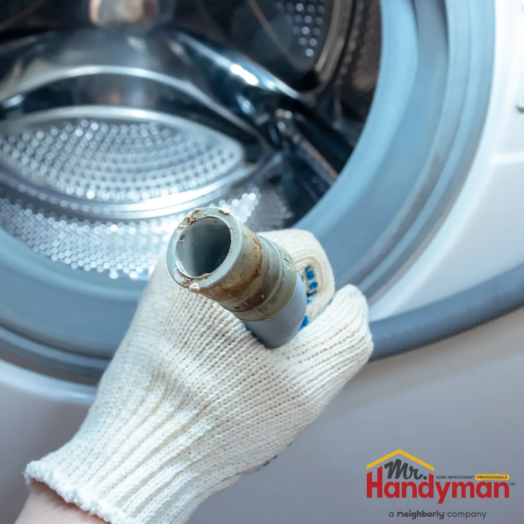A person holds up a gray washing machine drain hose.