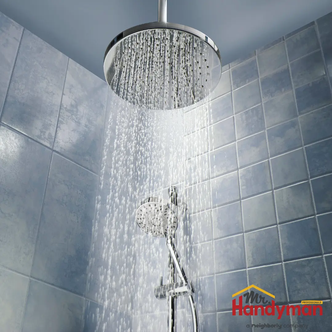 A chrome rain shower head sprays water downward against a background of blue wall tiles.