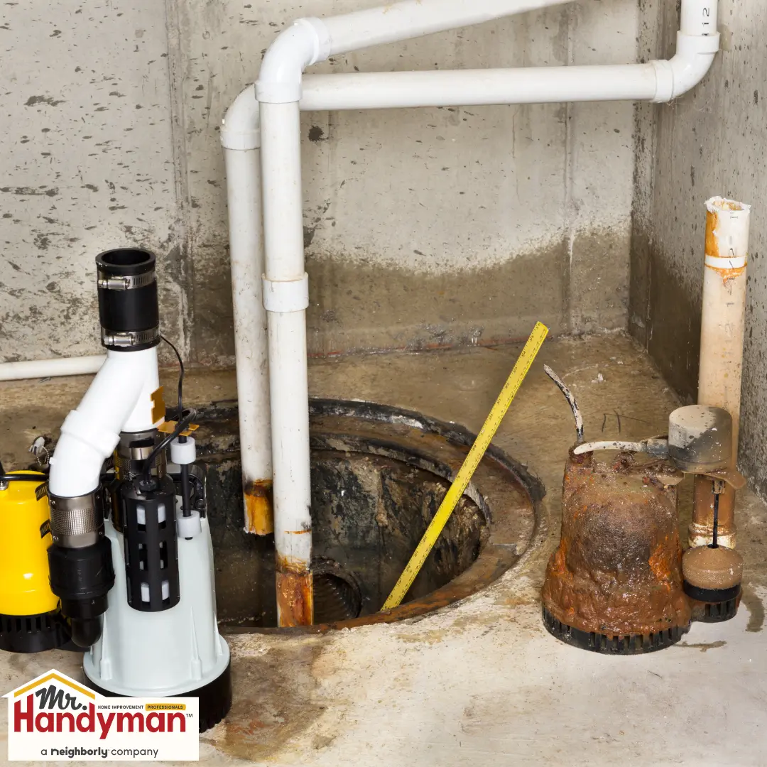 New white and yellow sump pump next to an old rusty one, both near an open sump pit with white pipes in a concrete basement.