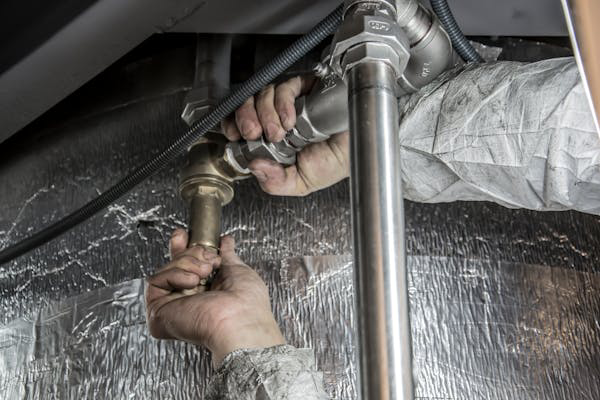 Photo of plumbing pipes. Two hands are working on the pipes.
