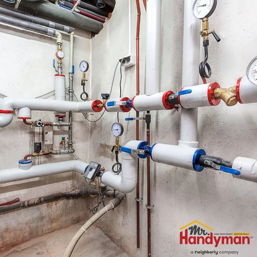 A boiler room plumbing system with multiple white PVC pipes, brass fittings, and pressure gauges mounted on a concrete wall.