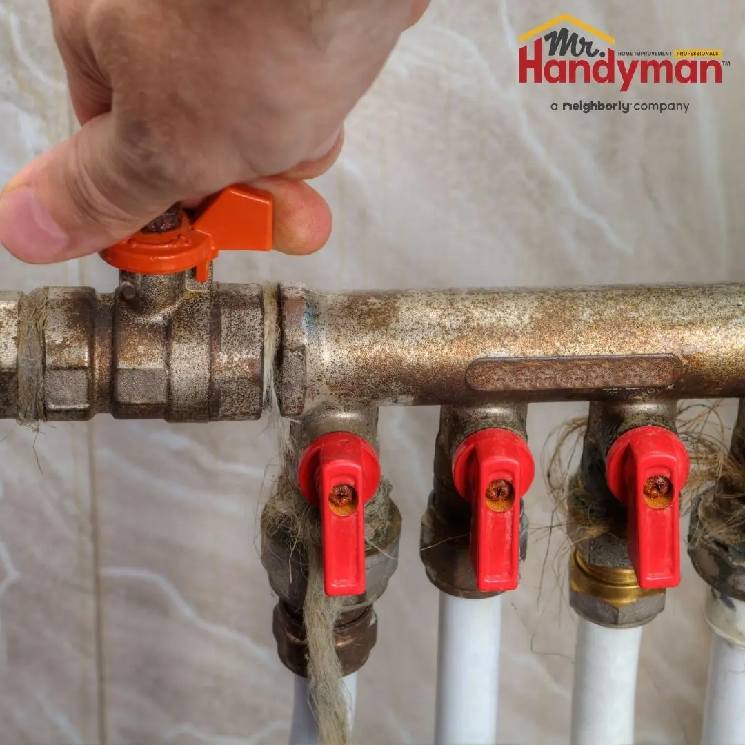 A person turning off a home water supply shut-off valve using a hand-operated handle.
