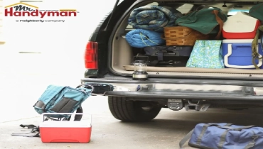 The open trunk of a vehicle packed with camping gear, including coolers, sleeping bags, and a lantern, alongside a backpack and duffel bag on the ground.
