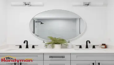 A modern bathroom featuring a grey vanity cabinet, a large round mirror, and sleek black faucets.