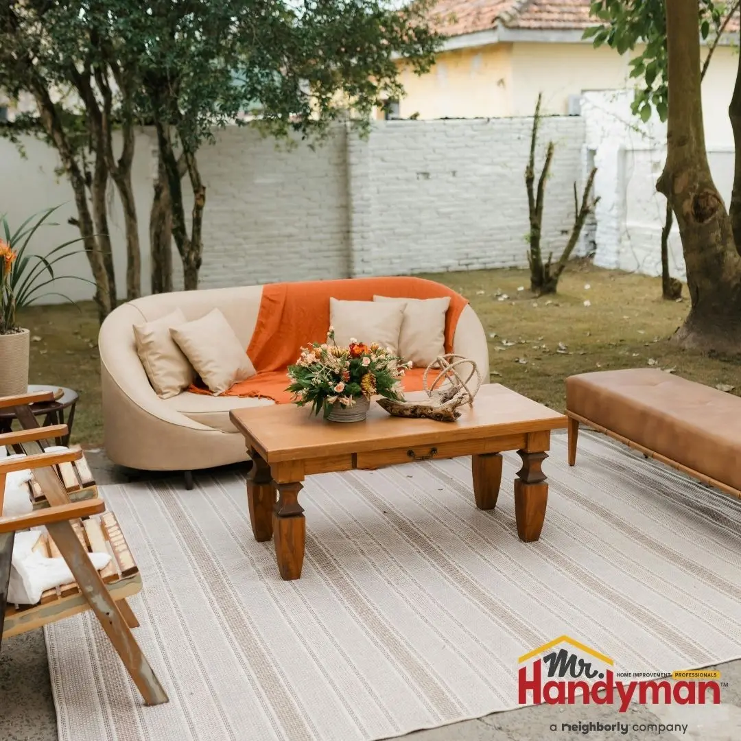 Curved beige sofa with orange throw blanket and wooden coffee table on a striped rug.