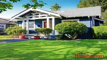 A blue house with white trim, featuring a well-kept front yard with manicured bushes and potted plants.