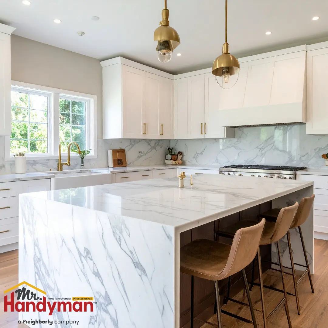 A modern kitchen features white cabinets, gold pendant lights, and a large marble island.