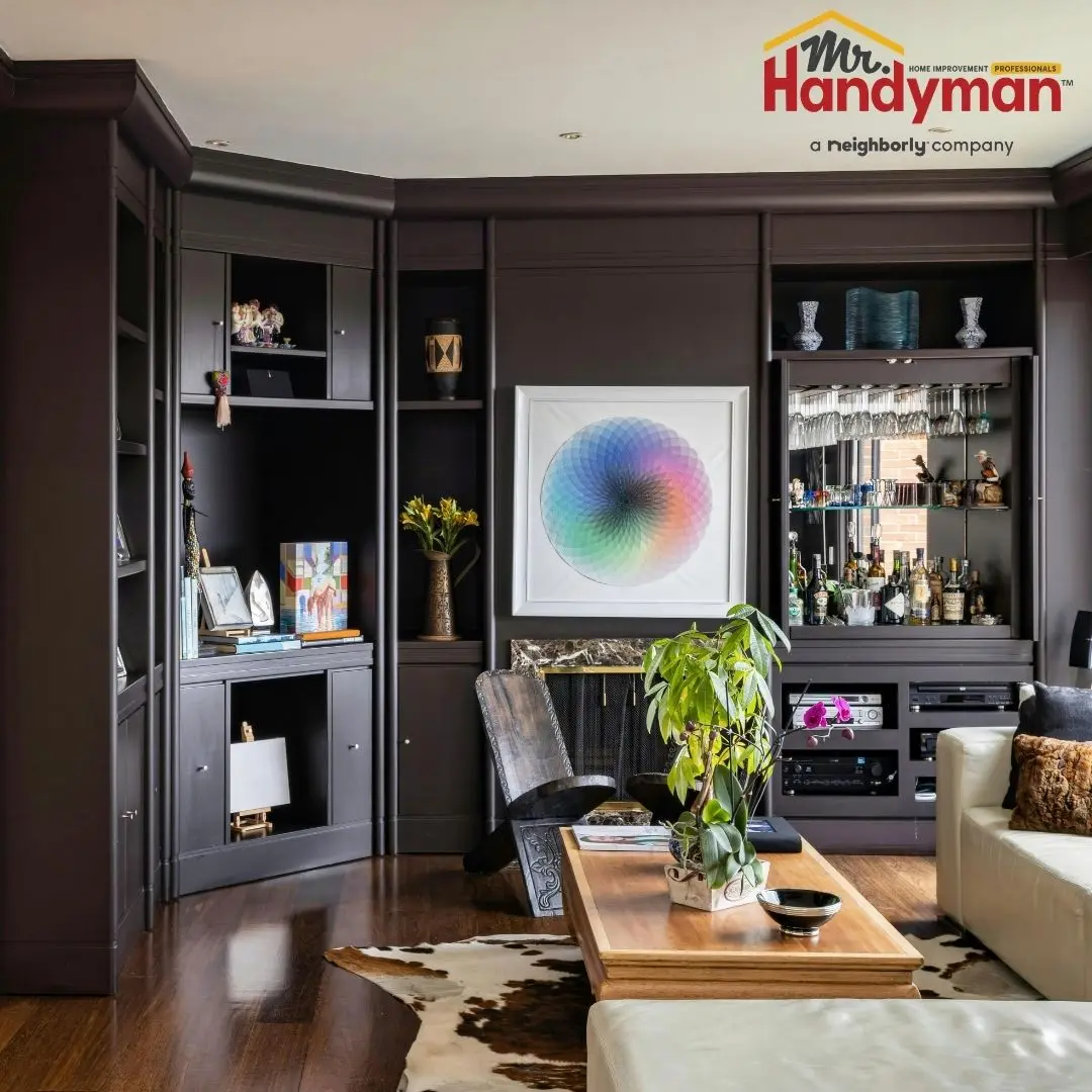 A modern living room featuring custom, dark-painted built-in cabinetry and a home bar setup.
