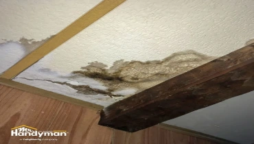 Water damaged ceiling with dark stains and cracks next to a wooden beam.