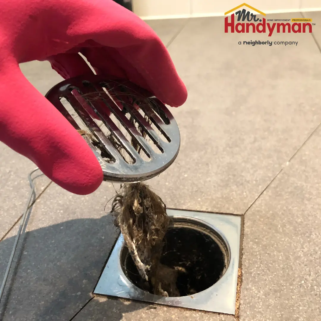 A person wearing gloves holding a strainer over a sink drain.