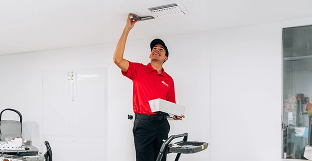 A Mr. Handyman® service professional on ladder repairing ceiling drywall damage using a trowel