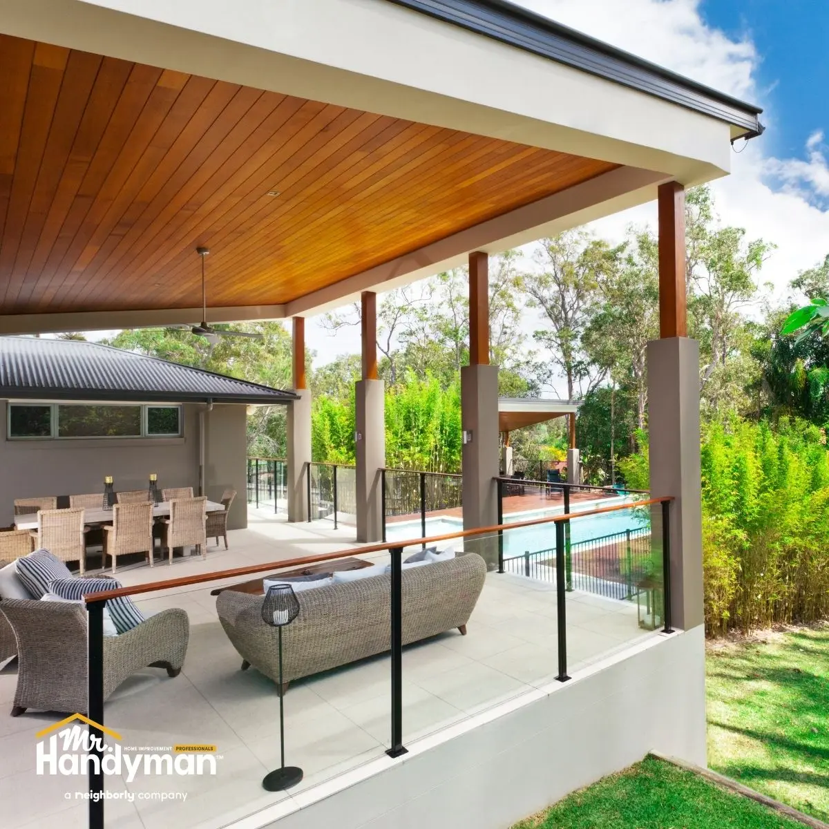 A covered patio with a wooden ceiling, outdoor seating, and a view of a pool and garden.