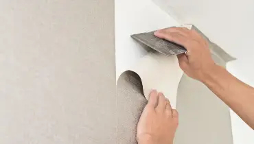 Handyman using a scraper to smooth out the wall where they are completing wallpaper repairs by installing a new sheet